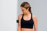 Mujer usando el rodillo Blackroll Mini negro para masajear el antebrazo junto a una puerta