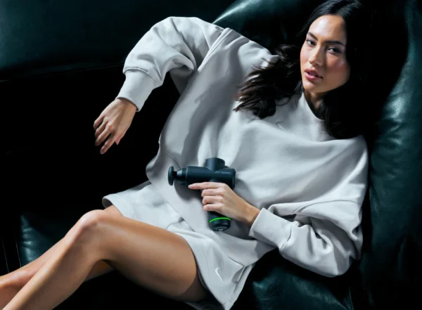 Mujer usando una pistola de masaje Hyperice sentada en un sillón
