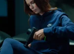 Mujer aplicando una pistola de masaje Hyperice en el antebrazo