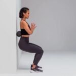 Mujer en sentadilla contra la pared usando el Duoball para masajear la espalda baja