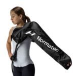 ALERTA -- imagen no corresponde al producto: muestra una bolsa de transporte Normatec al hombro de una persona, no el accesorio de brazos. Alt text descriptivo de lo que SÍ se ve: 'Mujer caminando al aire libre cargando al hombro una bolsa de transporte negra con logo Normatec'. Revisar asignación de imagen antes de usar.