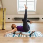 Mujer haciendo ejercicio de core sobre un mat de yoga, con el Giboard al fondo de la sala