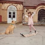 Niña jugando sobre el Giboard mientras un perro golden retriever la observa