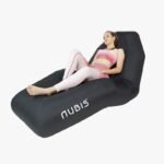 Mujer reclinada sobre la Silla Nubis Recovery Chair negra, vistiendo top y calzas deportivas rosadas y blancas, con las piernas extendidas