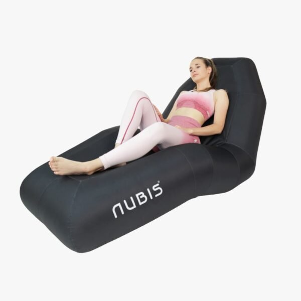 Mujer reclinada sobre la Silla Nubis Recovery Chair negra, vistiendo top y calzas deportivas rosadas y blancas, con las piernas extendidas