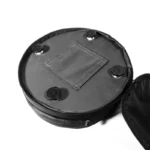 Vista superior del Taburete Nubis Stool plegado dentro de su bolso de transporte negro circular, con cuatro patas de goma y compartimento con cierre