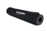 Mujer arrodillada sobre el mat Blackroll sosteniendo una pelota de masaje verde
