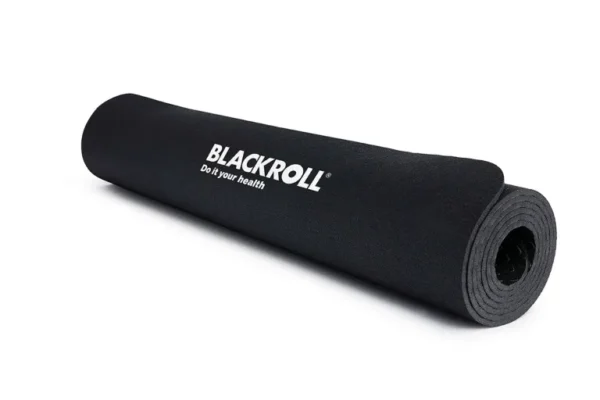 Mujer arrodillada sobre el mat Blackroll sosteniendo una pelota de masaje verde