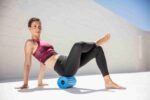 Mujer usando Blackroll Groove Pro azul para liberación miofascial de glúteo, sentada en el suelo