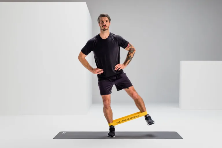 Hombre haciendo paso lateral con Blackroll Loop Band alrededor de los tobillos