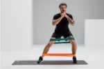 Hombre haciendo sentadilla con dos Blackroll Loop Band (naranja y verde) sobre las rodillas