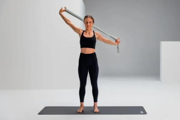 Mujer usando Blackroll Stretch Band verde para apertura de hombro y pecho, brazos en alto