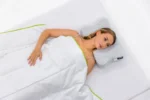 Vista cenital de mujer bajo la manta, apoyada sobre la almohada con funda Allergoprotect