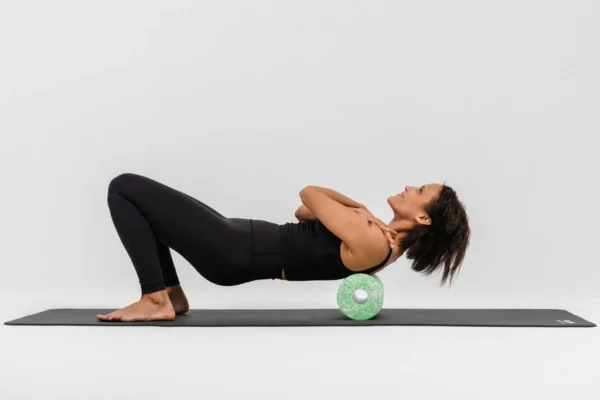 Mujer en posición de puente con la Ball 12 verde bajo la zona lumbar, sobre un mat de yoga