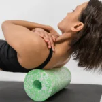 Mujer en posición de puente sobre el rodillo Med de Blackroll, con las manos entrelazadas detrás del cuello, trabajando la zona dorsal