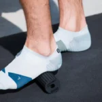 Pies con calcetines deportivos apoyados sobre el rodillo Mini Flow negro, en el suelo