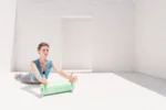 Mujer sentada en el suelo apoyando la mano sobre el rodillo Med 45 verde, en una sala blanca