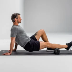 Hombre sentado apoyando la zona lumbar sobre el Blackroll Twin, sobre mat de entrenamiento