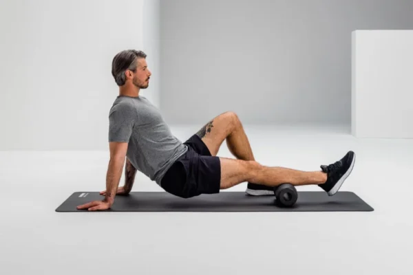 Hombre sentado apoyando la zona lumbar sobre el Blackroll Twin, sobre mat de entrenamiento
