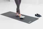 Pies descalzos sobre mat de yoga junto a zapatillas, ejercicio de movilidad de pie