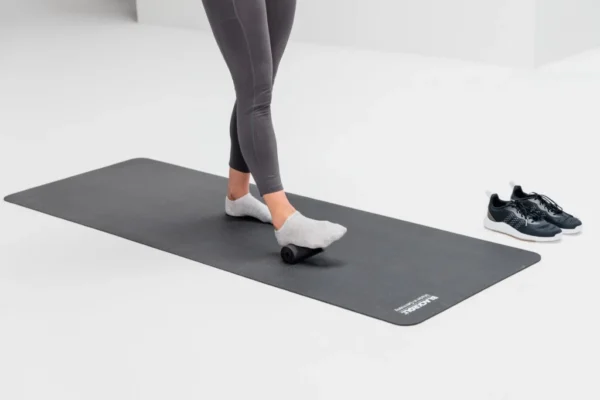 Pies descalzos sobre mat de yoga junto a zapatillas, ejercicio de movilidad de pie