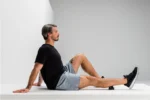 Hombre sentado con la pierna extendida en posición de estiramiento, sobre un mat