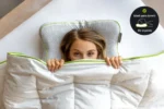Vista cenital de mujer asomada bajo la manta con la Blackroll Recovery Pillow detrás de la cabeza