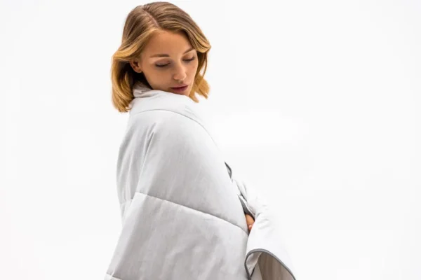 Mujer envuelta en la Blackroll Recovery Blanket Summer sobre los hombros, de perfil