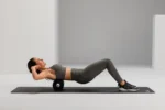 Mujer haciendo abdominales con el rodillo Standard 45 apoyado bajo la espalda alta, sobre un mat oscuro