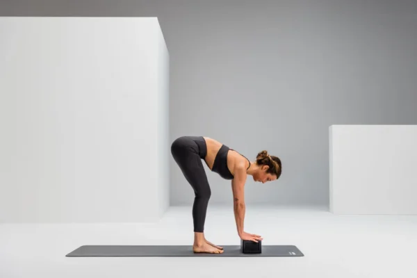 Mujer en postura de flexión hacia adelante con las manos apoyadas sobre el Block, sobre mat de yoga