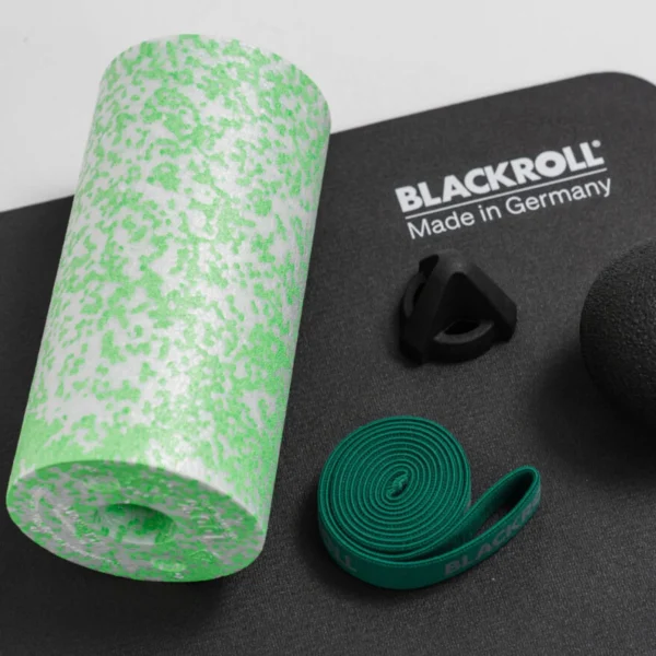 Vista superior del rodillo Med verde/blanco, el Trigger negro y la Super Band verde del kit Back Box, sobre una superficie negra con el texto BLACKROLL Made in Germany