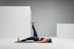 Mujer acostada boca arriba con una pierna elevada, usando el Blackroll Block como apoyo lumbar