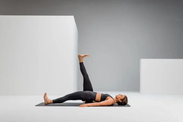Mujer acostada boca arriba con una pierna elevada, usando el Blackroll Block como apoyo lumbar