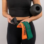 Mujer sosteniendo el Trigger negro y las Loop Band naranja y verde, con el rodillo Twin bajo el brazo