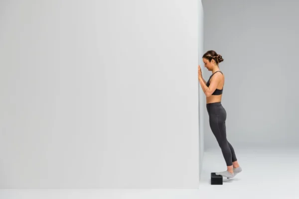 Mujer haciendo elevación de talón apoyada contra la pared con el Blackroll Block bajo el pie