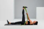 Mujer acostada boca arriba usando la Multi-Band verde para estirar la pierna extendida hacia arriba