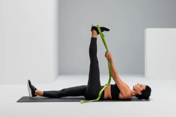 Mujer acostada boca arriba usando la Multi-Band verde para estirar la pierna extendida hacia arriba