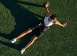 Vista aérea de una mujer recostada en el pasto usando el Normatec Elite Cadera en la cintura, con el logo Hyperice y el texto Normatec visibles en la prenda