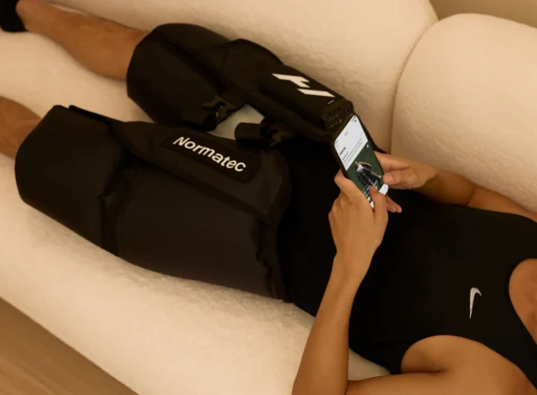 Persona recostada en un sillón usando el Normatec Elite Cadera, revisando la sesión desde la Hyperice App en su teléfono