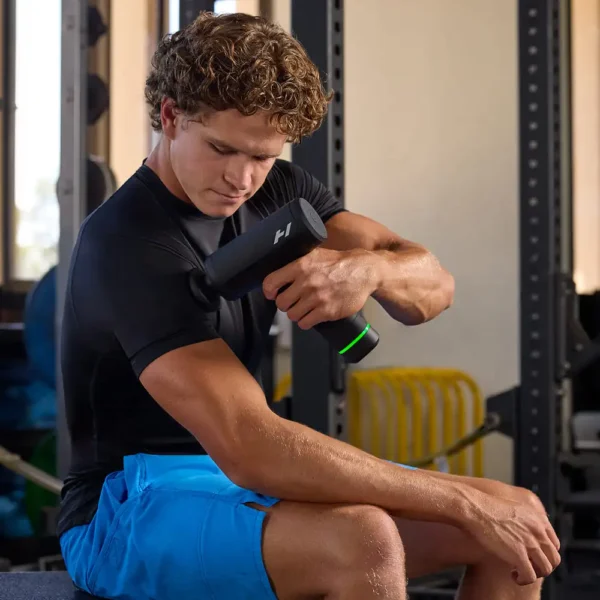 Hombre usando Hypervolt 3 Pro en el brazo, sentado en un banco de gimnasio