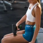 Primer plano de mujer usando Hypervolt Go 3 en la pierna, sentada en banco de gimnasio